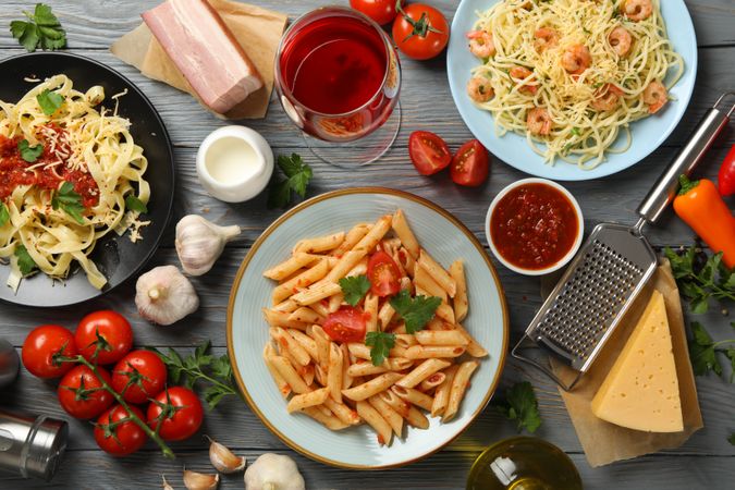 Composition with plate of tasty pasta and ingredients for cooking on wooden background