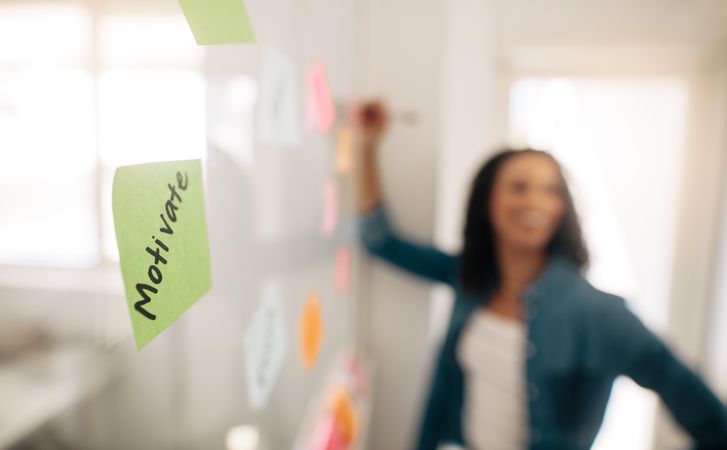Sticky note on board with word “Motivate” with female manager in background