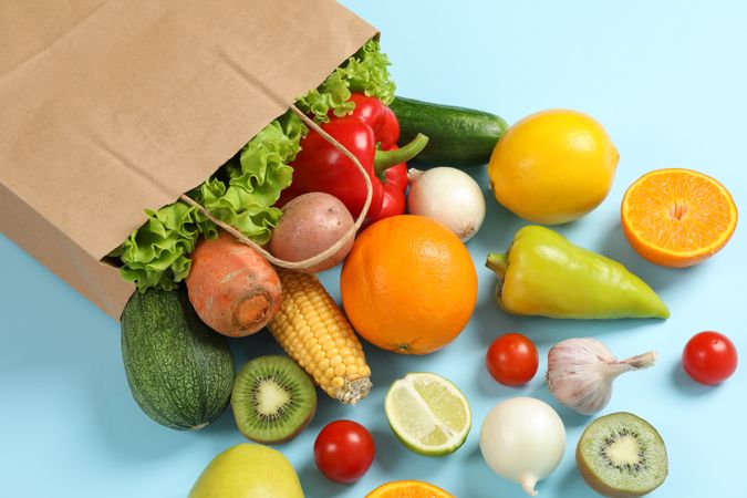 Paper bag, vegetables and fruits on blue background, space for text