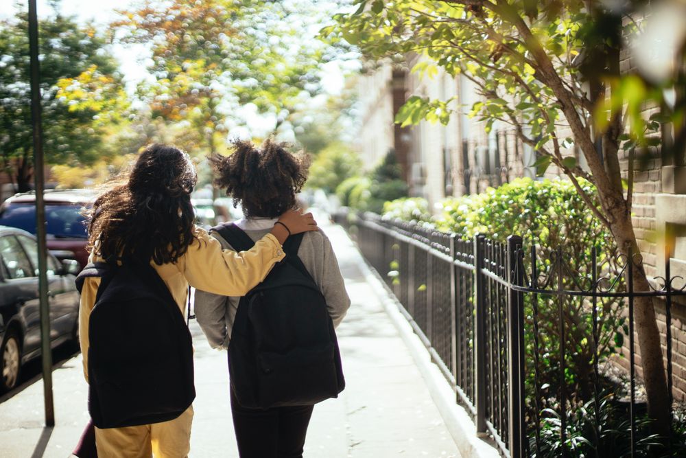 Back view of two students with backpacks walking on sidewalk