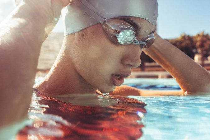 Close up of young woman swimmer inside the swimming pool adjusting her goggles