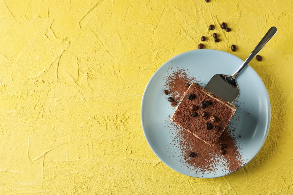Plate with delicious tiramisu on yellow background. Tasty dessert