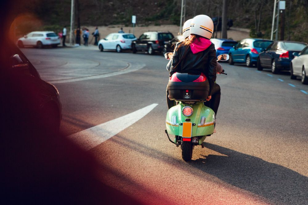 Unrecognizable figures riding scooter on road