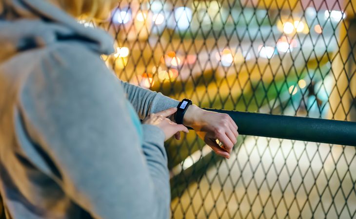 Unrecognizable female hands touching digital wrist band to check step counter after walking at night