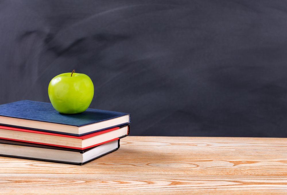 Back to school books and green apple in front of erased chalkboard