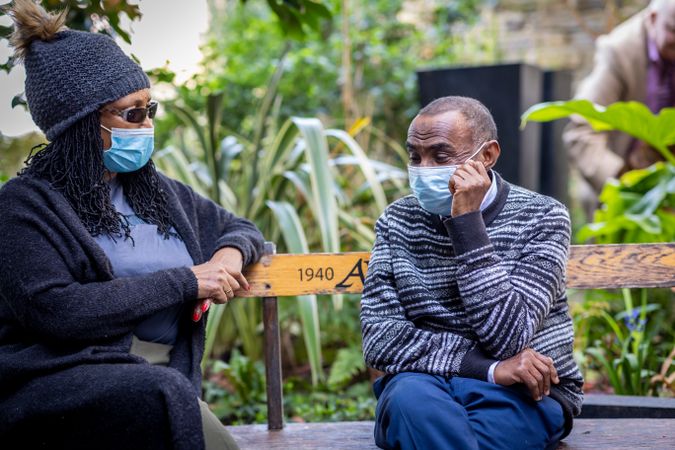 Mature Black man and woman sitting outside talking on a park bench