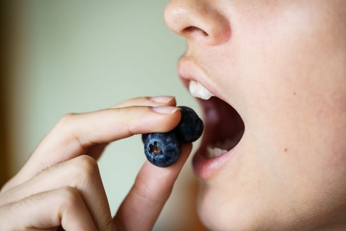 Side view of teenage girl with mouth open eating fresh blueberries