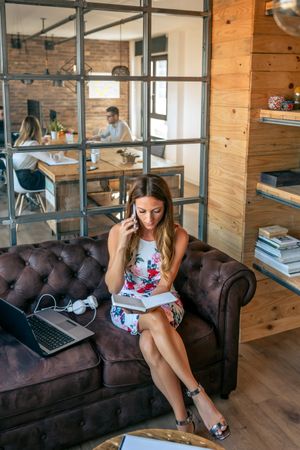 Busy businesswoman working with laptop talking on the phone sitting on the sofa