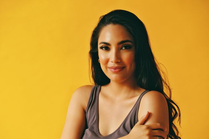 Calm happy Hispanic woman looking at camera in yellow room, copy space