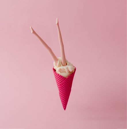 Doll legs emerging from vanilla ice cream in pink waffle cone on pink pastel background