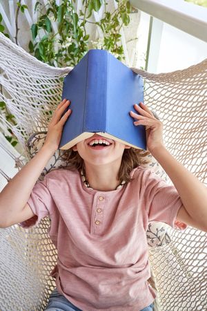 Unrecognizable boy lying in hammock with book on head