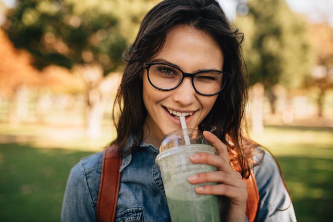 Cheerful woman at park drinking juice and winking