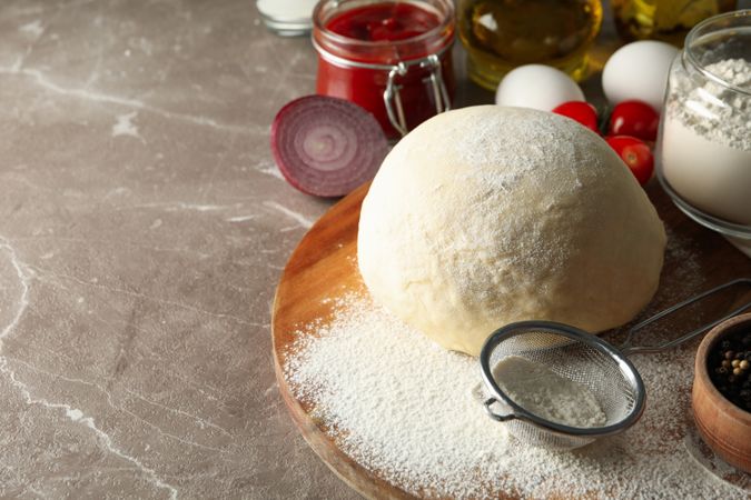 Dough and ingredients for cooking pizza on gray background
