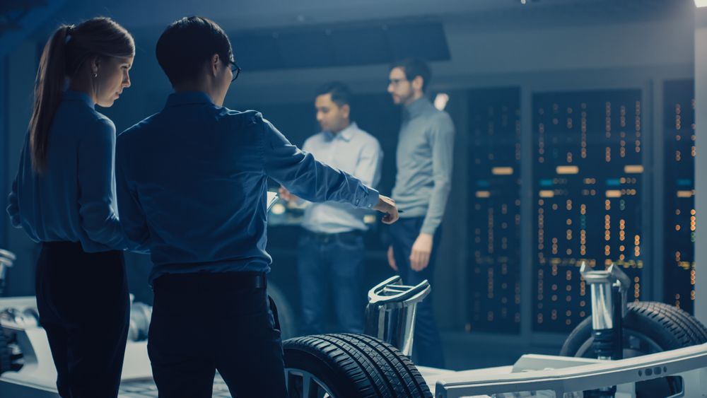 Automobile Engineers Discussing and Designing Electric Car Chassis Platform, Using Tablet Computers with 3D CAD Software