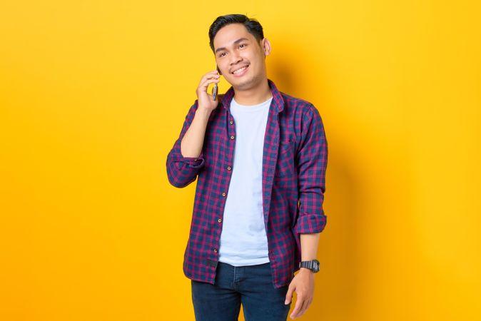 Asian male talking on cell phone in yellow studio shoot