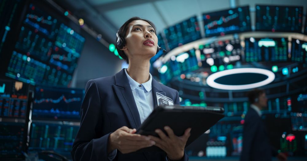Young Female Stock Exchange Broker Working on Tablet Computer with Real-Time Stocks, Commodities and Exchange Market Charts. Professional Asian Investment Agent in Modern Office Building.