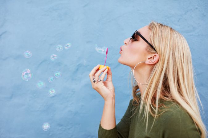 Side view shot of attractive female model blowing soap bubbles