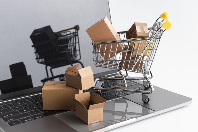 Shopping Concept With Mini Cart and Boxes on Laptop Displaying E-commerce
