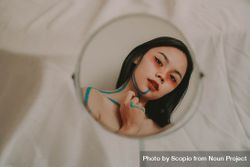Reflection of woman drawing on herself with blue marker on round mirror 4A8g65