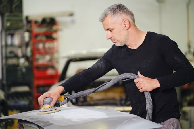 Mechanic grinding paint from car detail