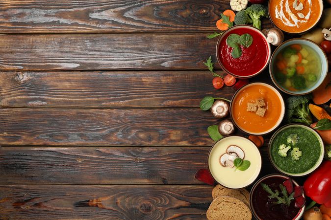 Top view of colorful soups on right side of dark wooden table with copy space