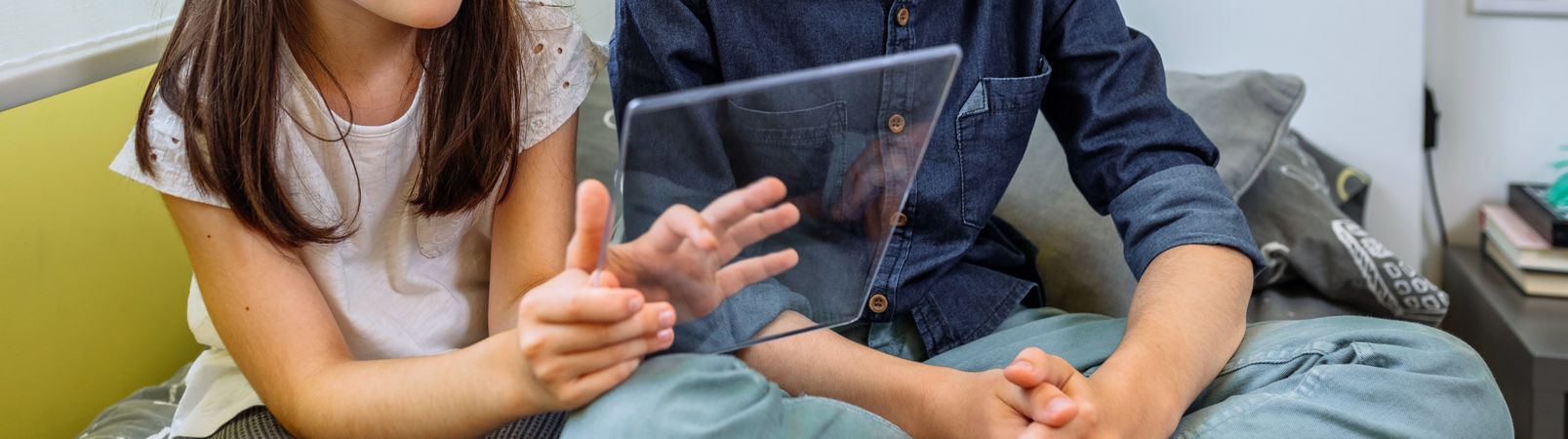 Banner of unrecognizable children having fun with futuristic transparent tablet sitting over bed.