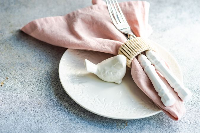 Easter table setting on concrete background with bird figurine and pink napkin