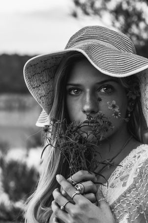 Grayscale photo of woman wearing hat holding flowers