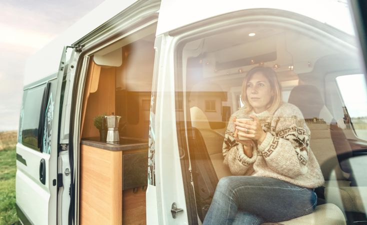 Female in cozy sweater sipping coffee in van through glass reflection
