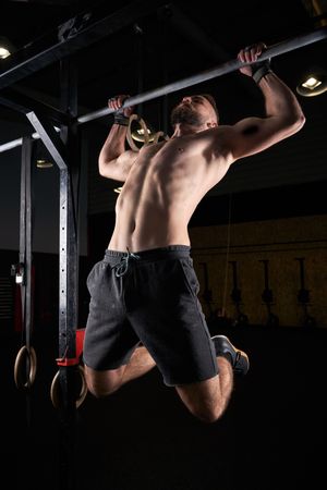 Shirtless sportsman doing pull ups on bar
