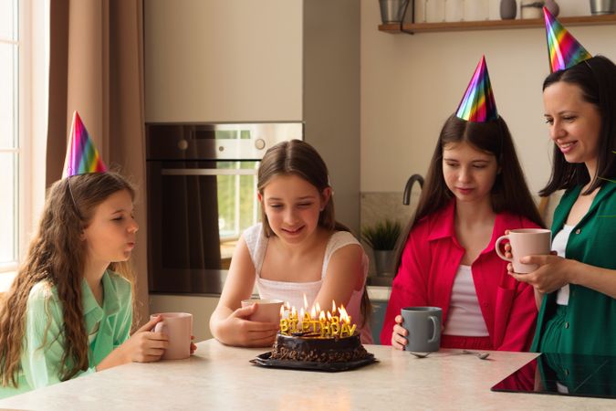 Family celebrating young girl's birthday with cake and party hats