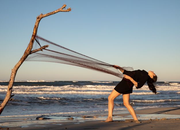 Woman in fishing net fixed on twig near water on shore