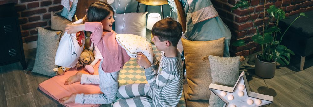 Banner of excited boy and girl laughing and playing in cushion battle on teepee