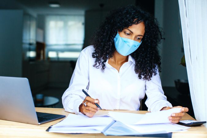 Woman working on documents with a laptop while wearing a facemask