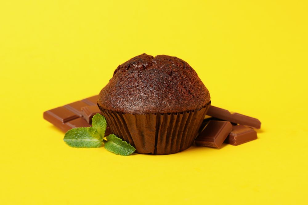 Tasty muffin and chocolate on yellow background