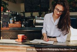 Female making notes in her book while relaxing at coffee shop 56yOV0