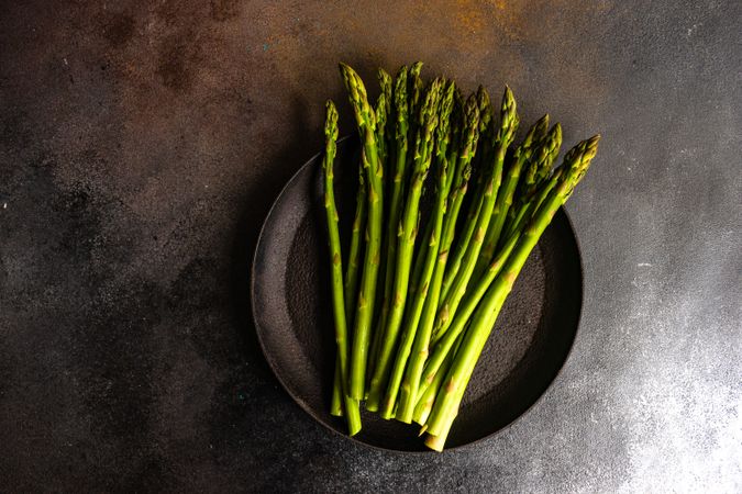 Raw asparagus on dark plate and dark counter with copy space