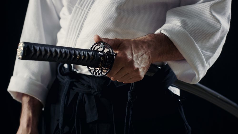 Aikido Master Wearing Traditional Samurai Hakama Clothes Holds His Japanese Sword in Scabbard.