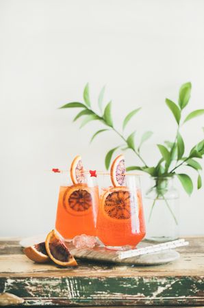 Two glasses of an orange cocktail with blood orange slices, and leaves in background