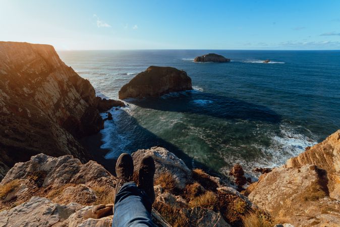 Person sitting on cliff near water