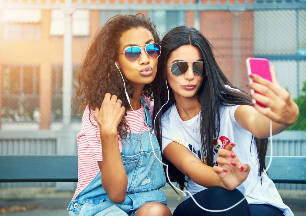 Two female adults posing for selfie on smart phone