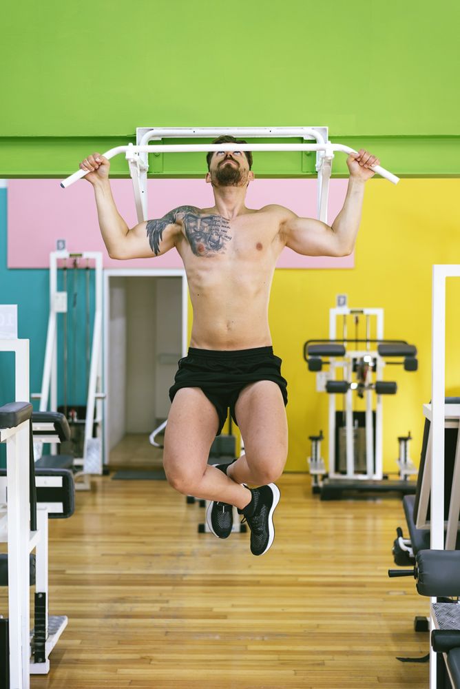 Front of man working out shoulders in a fitness club on pull up bar