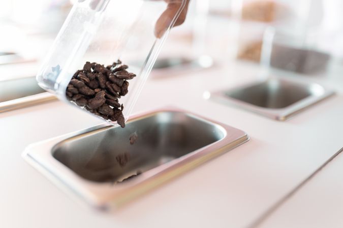 An ice-cream parlor worker is dropping some chocolate cereals into the counter tray