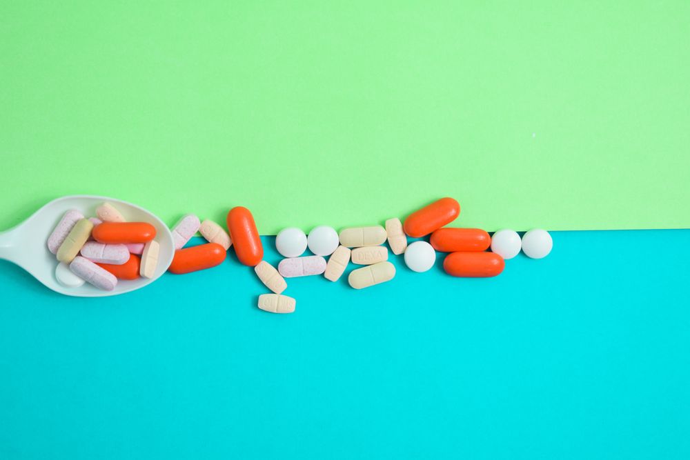 Scattered pills with plastic spoon on duo tone green and blue table