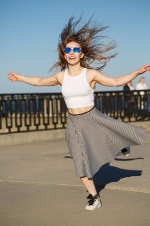 Smiling female in striped skirt joyously dancing near water