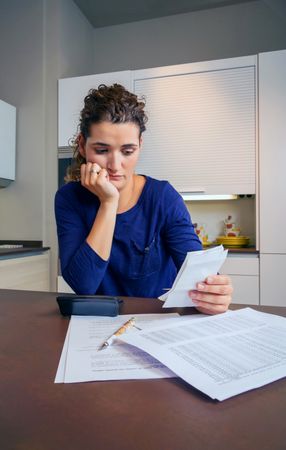 Tense woman reviewing bills at kitchen counter