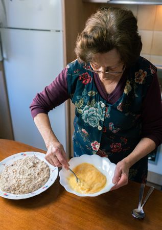 Mature woman beating eggs at home making handmade croquettes