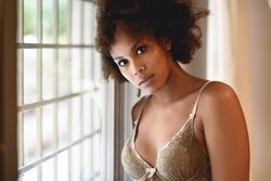 Female with curly hair in underwear leaning on window