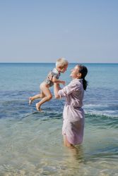 Woman and small kid having fun with water while relaxing on seacoast at resort