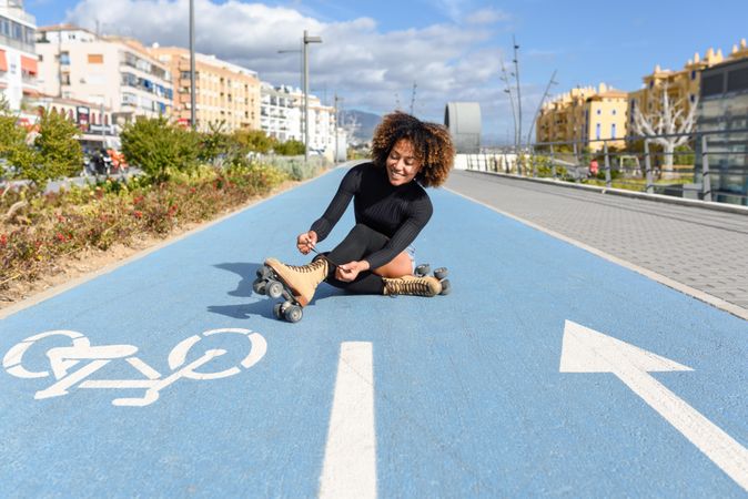 Smiling female in roller skates sitting in bike lane on nice day